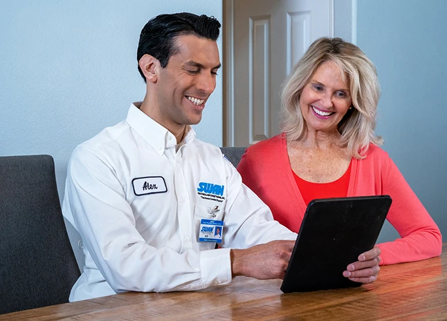 Swan Plumbing, Heating, and Air technician Alex reviews service options with a smiling customer at a table using a tablet.