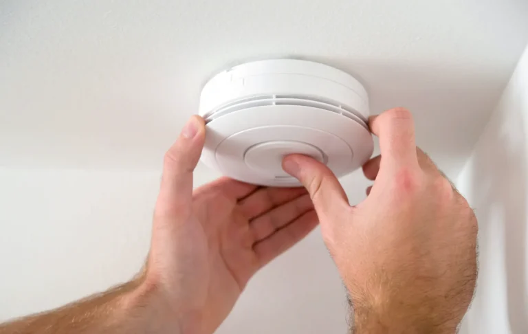 A Swan Plumbing, Heating, and Air team member checking a smoke detector on a white ceiling to ensure home safety.