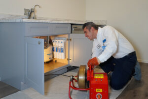 %Imagetitle% | Swan Plumbing, Heating, Electric &Amp; Air Conditioning A Swan Plumbing, Heating, and Air technician uses drain cleaning equipment to inspect pipes under a kitchen sink with filtration system.